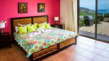 A bedroom with a large bed, a view of the outdoors, and a balcony with a grill.