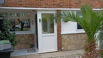 A brick building with a white door, a small garden area with gravel, and a palm plant.