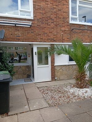 A brick building with a white door, a small garden area with gravel, and a palm plant.