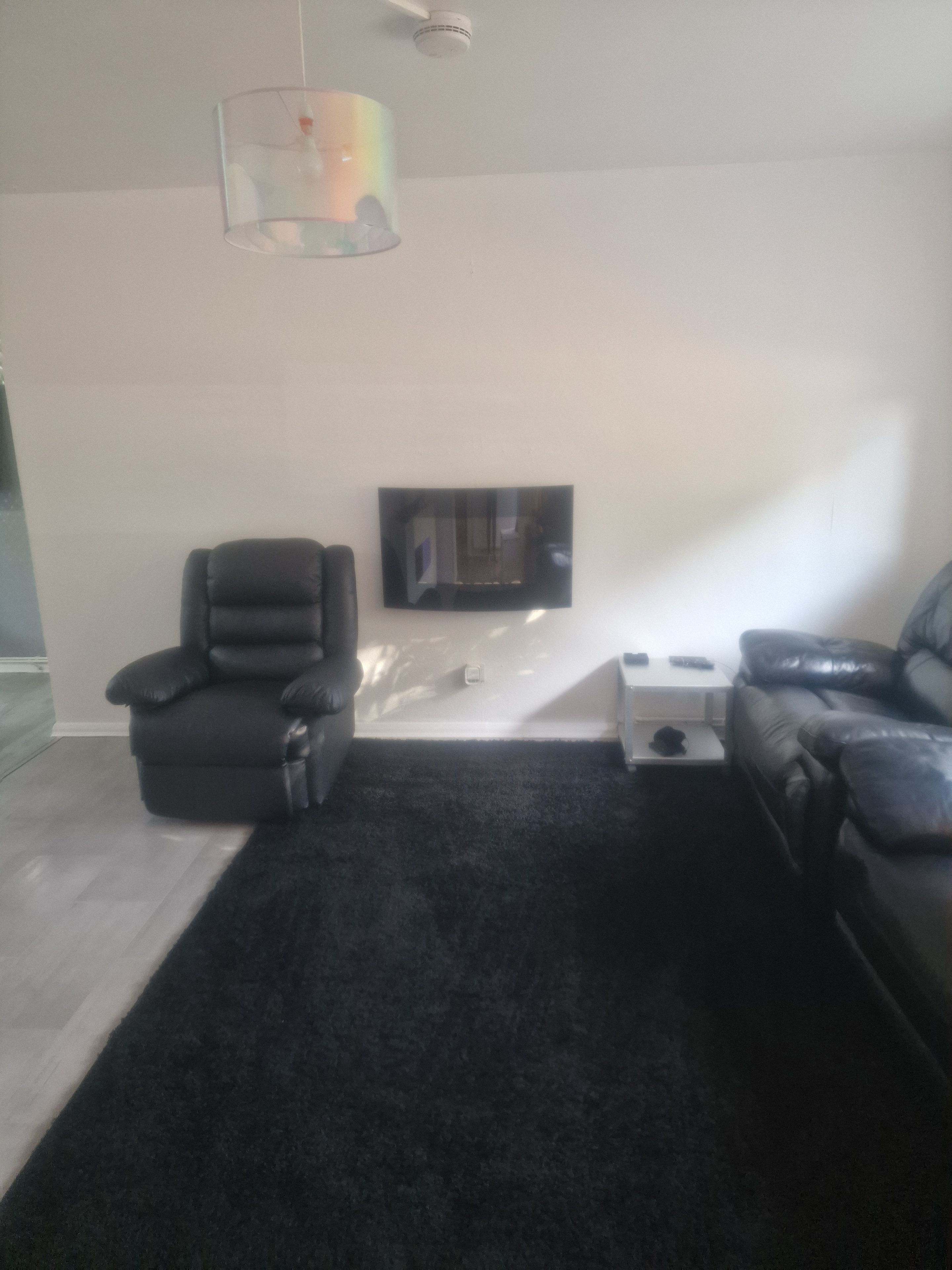 A living room with a black carpet, two leather sofas, a glass coffee table, and a mounted flat-screen TV.