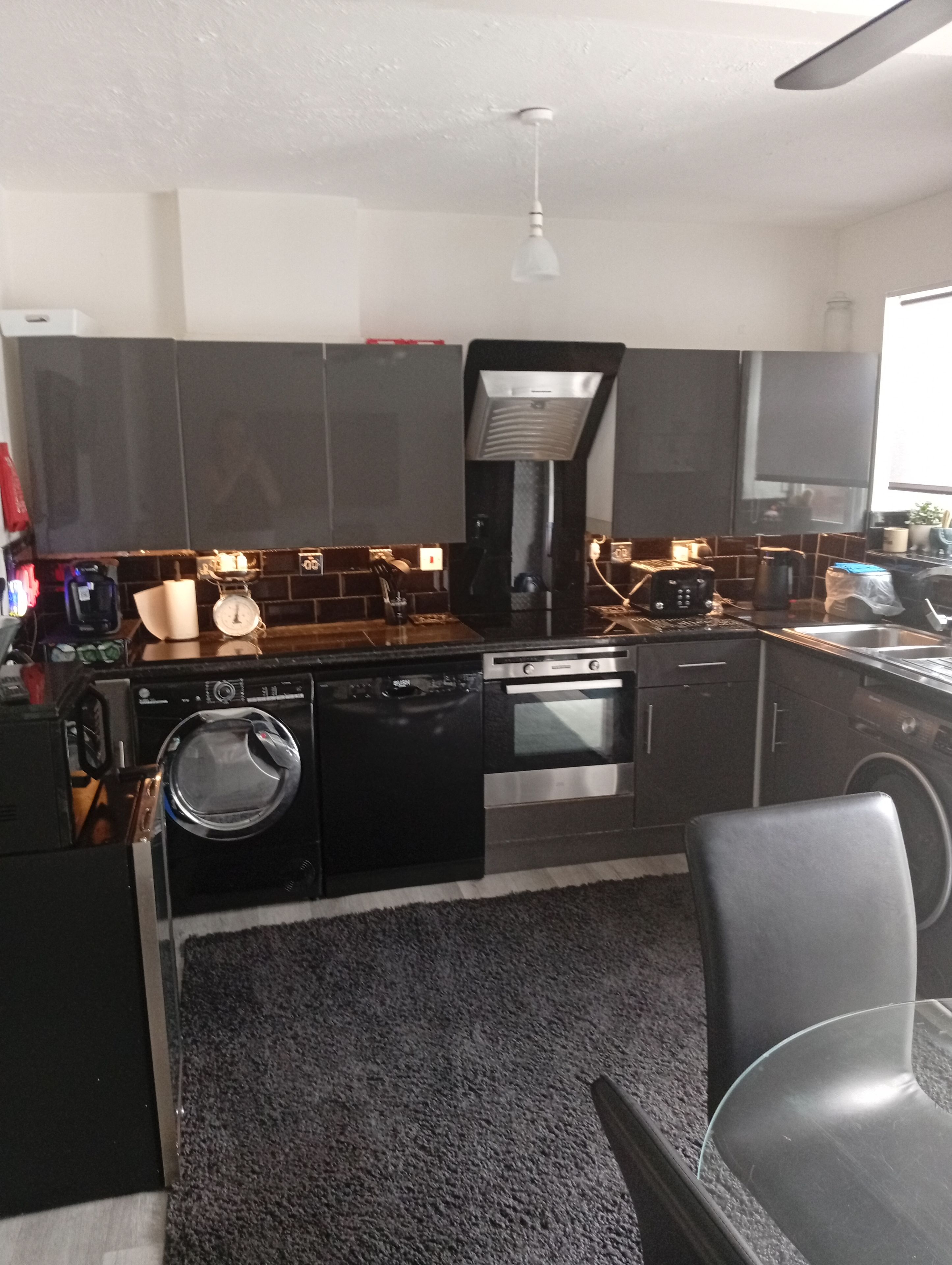 A modern kitchen with a dishwasher, oven, and microwave. There is a black countertop and a grey rug.