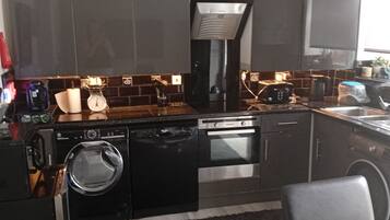 A modern kitchen with a dishwasher, oven, and microwave. There is a black countertop and a grey rug.
