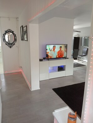 A modern living room with a flat-screen TV on a white entertainment unit, a black-framed mirror on the wall, and a black rug on the floor. - Garden flat, 2 beds, 20 mins to Central London (London)