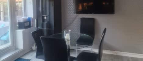 A modern dining area with a glass table, black chairs, a ceiling fan, and a flat-screen TV mounted on the wall.