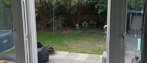 A view through a glass door into a backyard with a patio area, a tree, and a fence.
