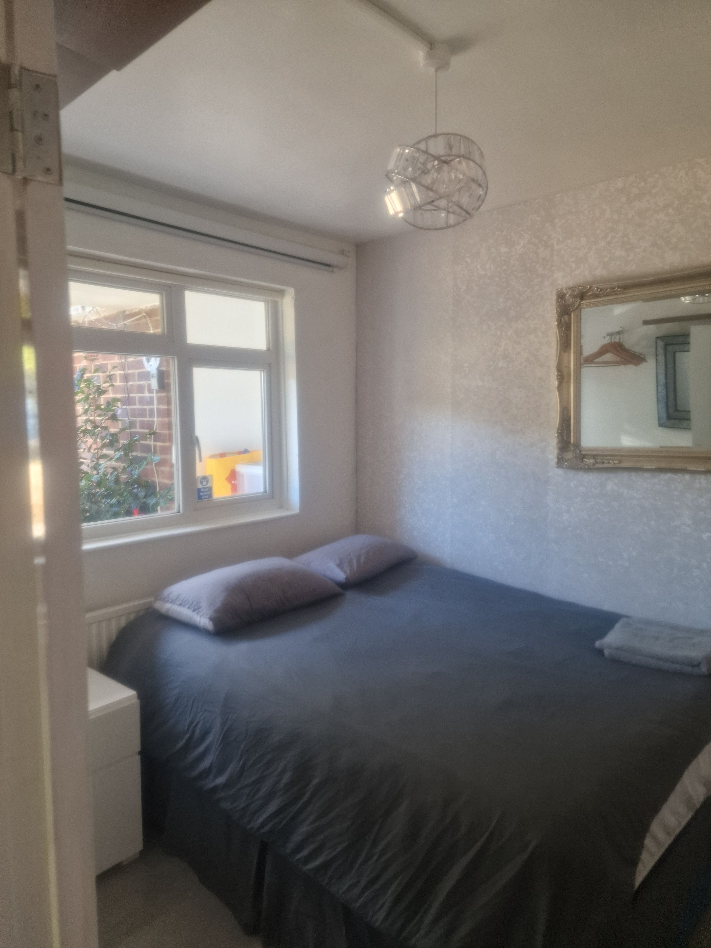 A bedroom with a bed, a window, a radiator, and a hanging light fixture.