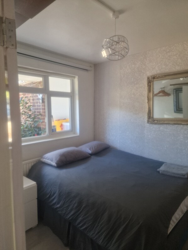 A bedroom with a bed, a window, a radiator, and a hanging light fixture.