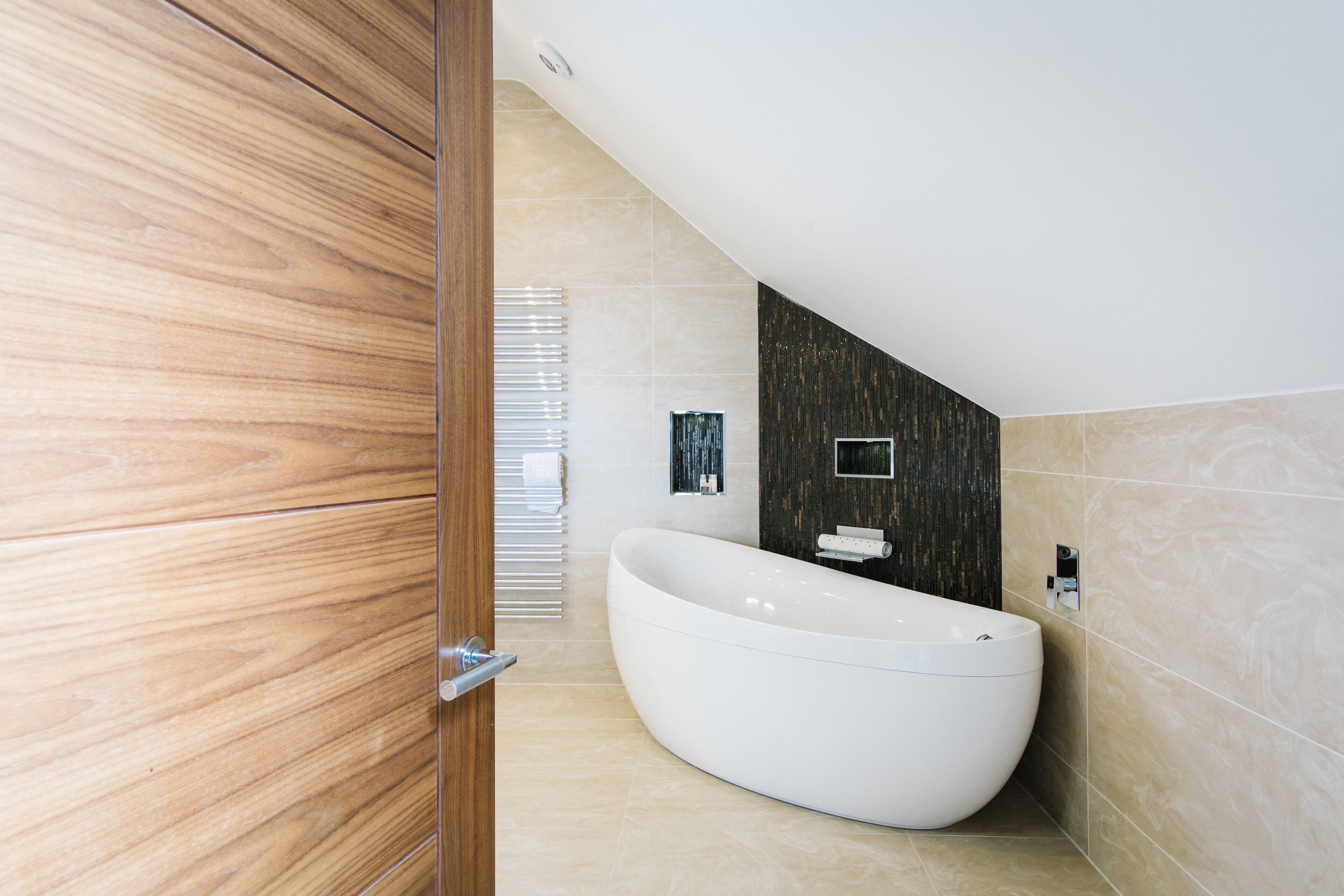 A modern bathroom with a freestanding bathtub, wooden flooring, and a sloped ceiling.