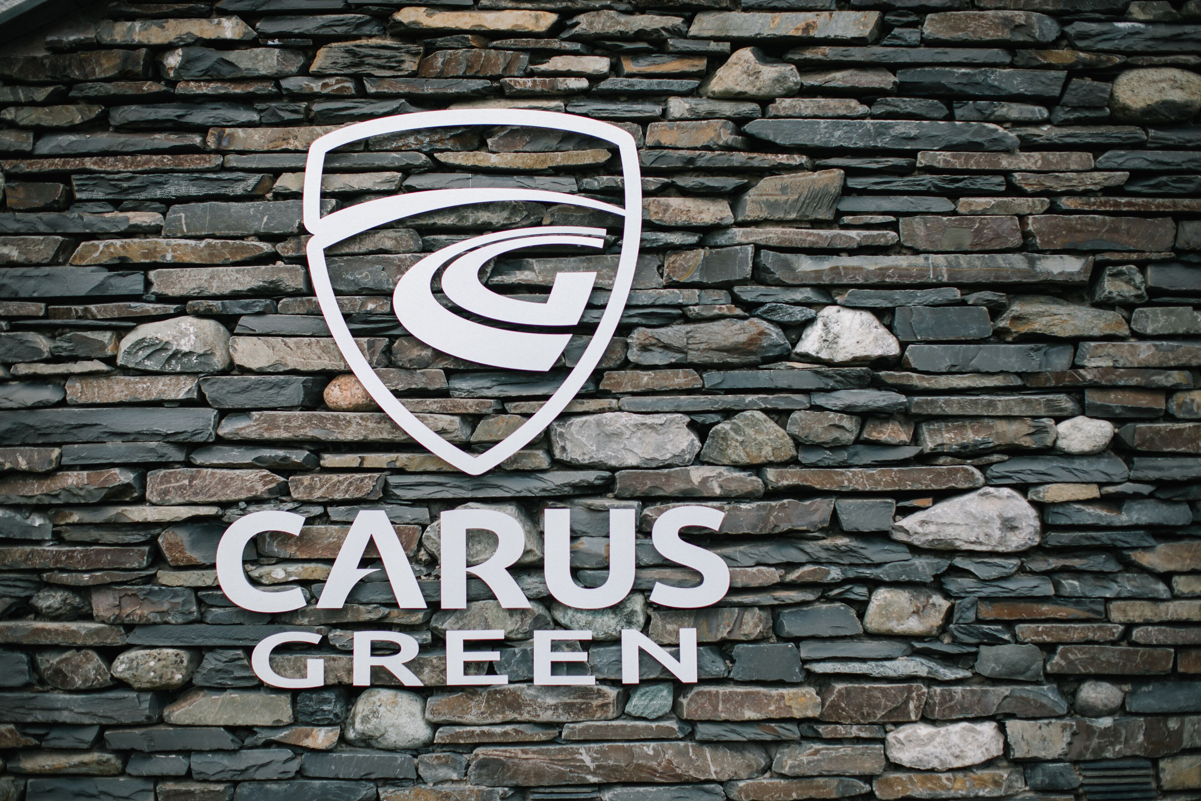 A logo with a stylized 'G' and the text 'CARUS GREEN' on a stone wall.