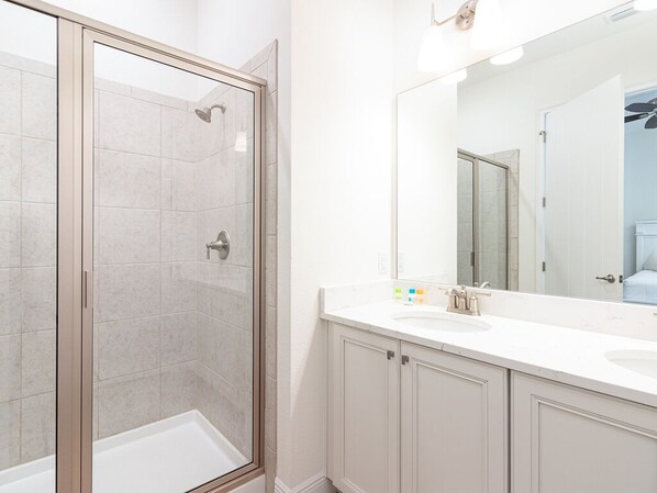 Un baño con ducha envuelta en vidrio, un espejo grande y un lavabo blanco con armarios.