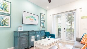 Una sala de estar con una pared verde azulado, una mesa de centro blanca, un sofá azul y una alfombra estampada.