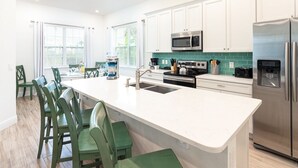 Una cocina moderna con armarios blancos, un refrigerador de acero inoxidable, un microondas y una isla grande con taburetes de bar.