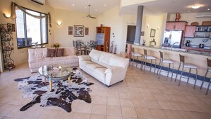 A spacious living room with a large white sofa, a glass coffee table, and a cowhide rug. There is a dining area with a bar and chairs. - Casa OM (Sardinal)