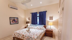 A bedroom with a bed, two bedside tables, a ceiling fan, an air conditioner, a window with curtains, and a wall-mounted picture. - Casa OM (Sardinal)