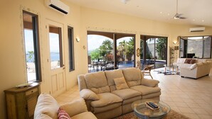 A spacious living room with a beige sofa, a glass coffee table, and a view of a pool and outdoor area. - Casa OM (Sardinal)