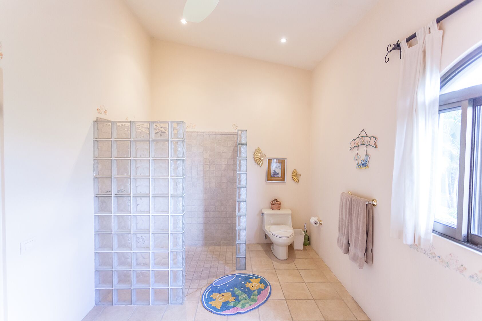Ein Badezimmer mit Duschkabine aus Glas, Toilette, Waschbecken und einem Fenster mit Vorhängen.