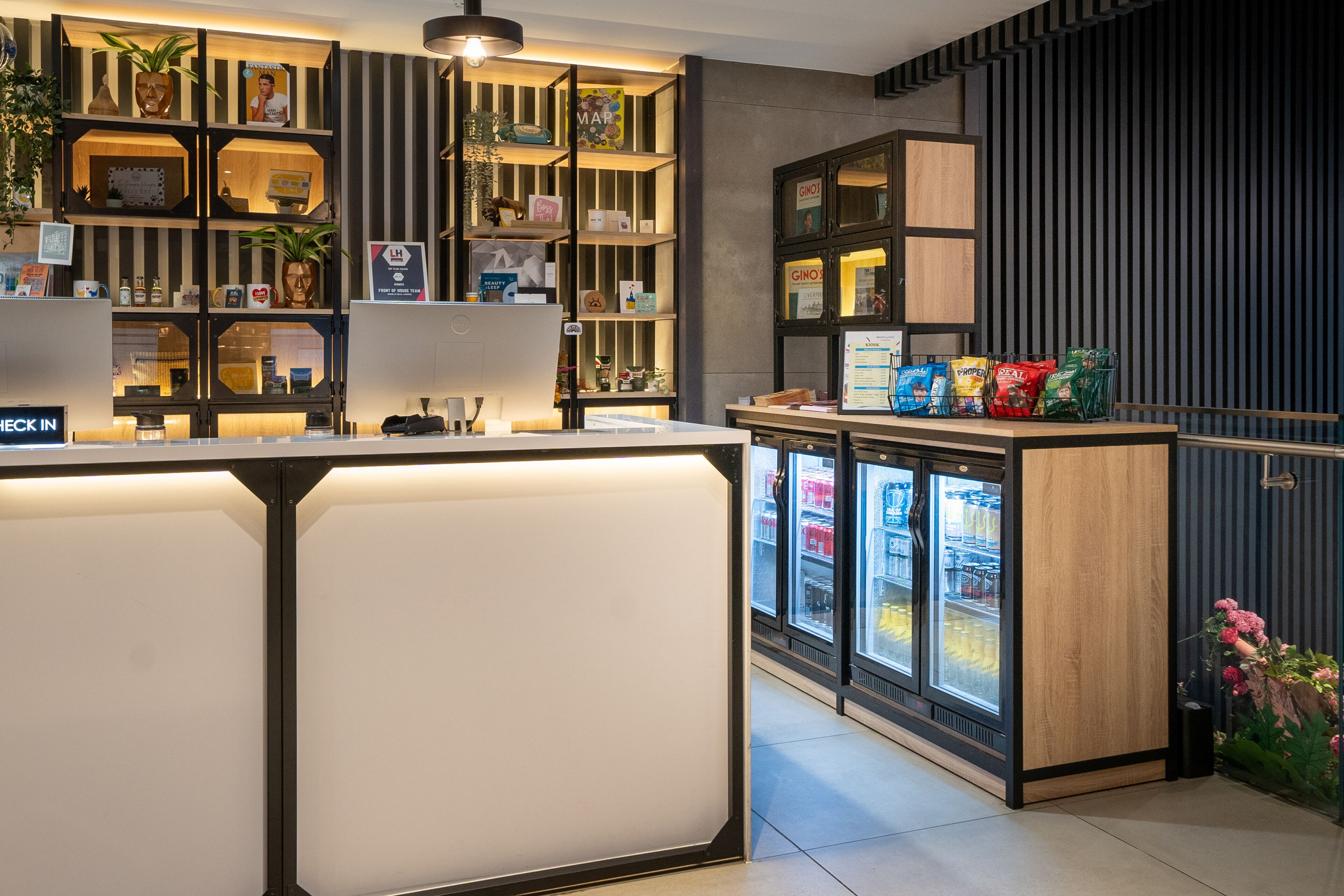 Una moderna zona de recepción con mostrador de entrada, una estantería ordenada y un expositor refrigerado.
