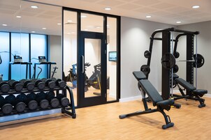 A gym with weightlifting equipment, treadmills, and a mirror wall.