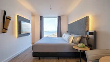 A modern hotel room with a large bed, a small table with a telephone, and a view of the sea.