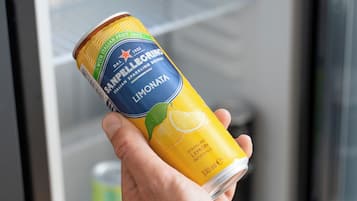 A hand holding a can of San Pellegrino Limonata Italian sparkling drink in front of a refrigerator.