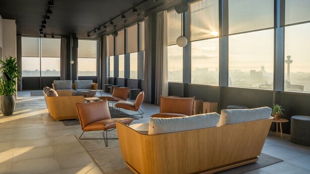 A modern lounge area with leather sofas and armchairs, large windows offering city views, and a potted plant. - INNSiDE by Meliá Liverpool (Liverpool)