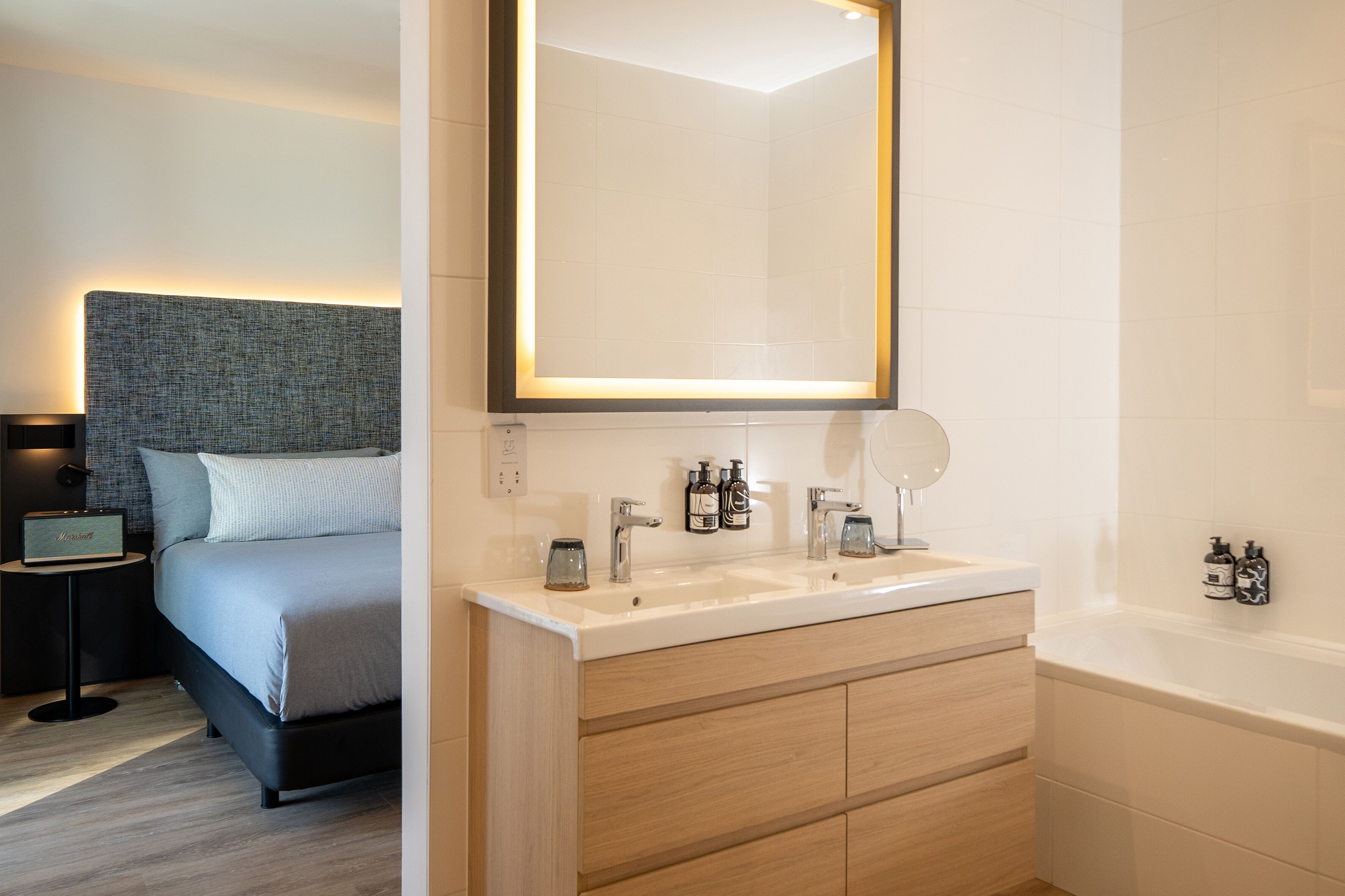 A modern bathroom with a large mirror, two sinks, a bathtub, and wooden cabinets.
