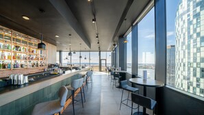 A modern bar area with a high ceiling, large windows, and a view of the cityscape. - INNSiDE by Meliá Liverpool (Liverpool)