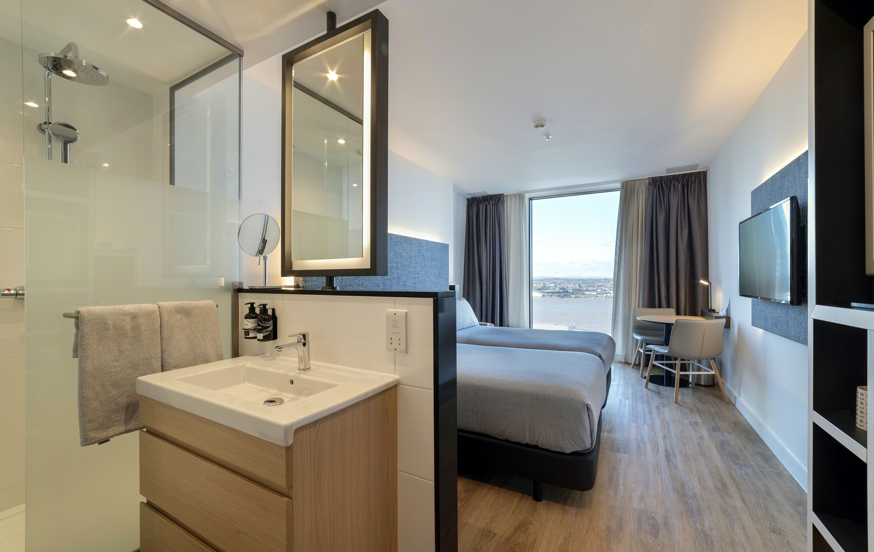 Une chambre d’hôtel moderne dotée d’un grand lit, d’un bureau, d’une télévision et d’une salle de bain avec un lavabo et un miroir.
