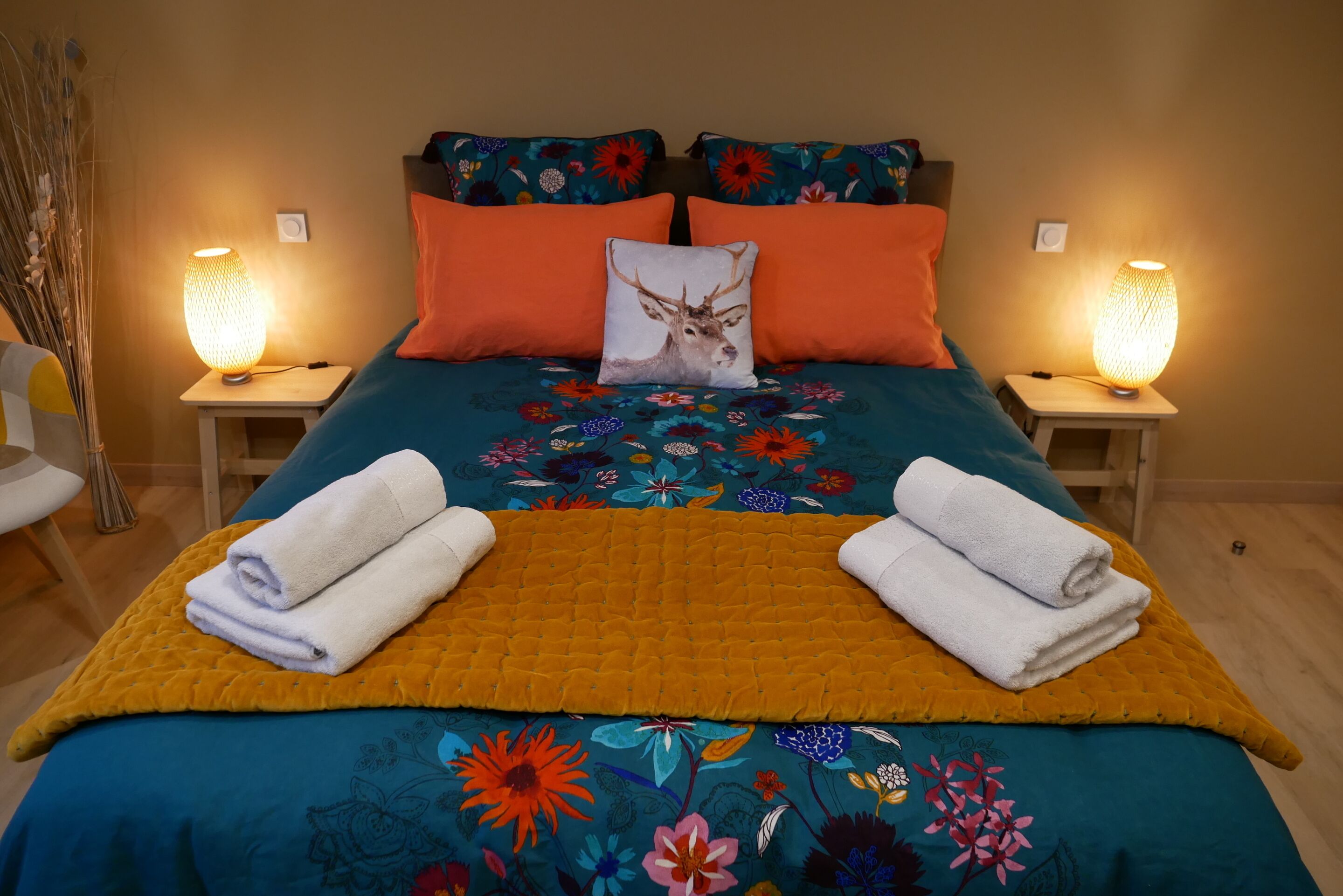 A neatly made bed with floral bedding, two pillows, and a decorative pillow with a deer.