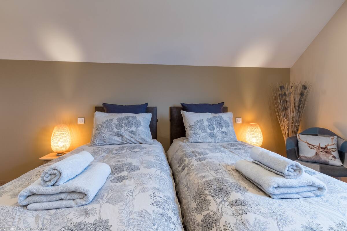 Habitación de hotel con dos camas, cada una con una toalla enrollada, ropa de cama floral a juego y lámparas de noche.