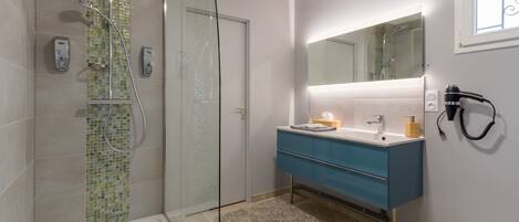 Un baño moderno con cabina de ducha de vidrio, una bañera blanca, un tocador azul con espejo y un inodoro blanco.
