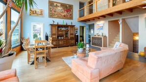 A spacious living area with a high ceiling, wooden flooring, a large painting, a dining set, and a staircase leading to an upper level. - Au Domaine du Cerf (Vyans-le-Val)