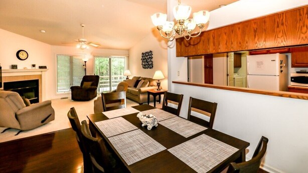 Ein modernes Wohnzimmer mit Kamin, einer Essecke mit Tisch für vier Personen und einer Küche mit Holzschränken und einem Kühlschrank.