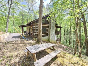Une cabane en bois avec une table de pique-nique, située dans une zone boisée.