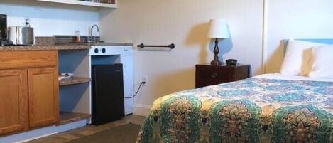 A compact room with a bed, a small kitchenette, and a wooden floor.