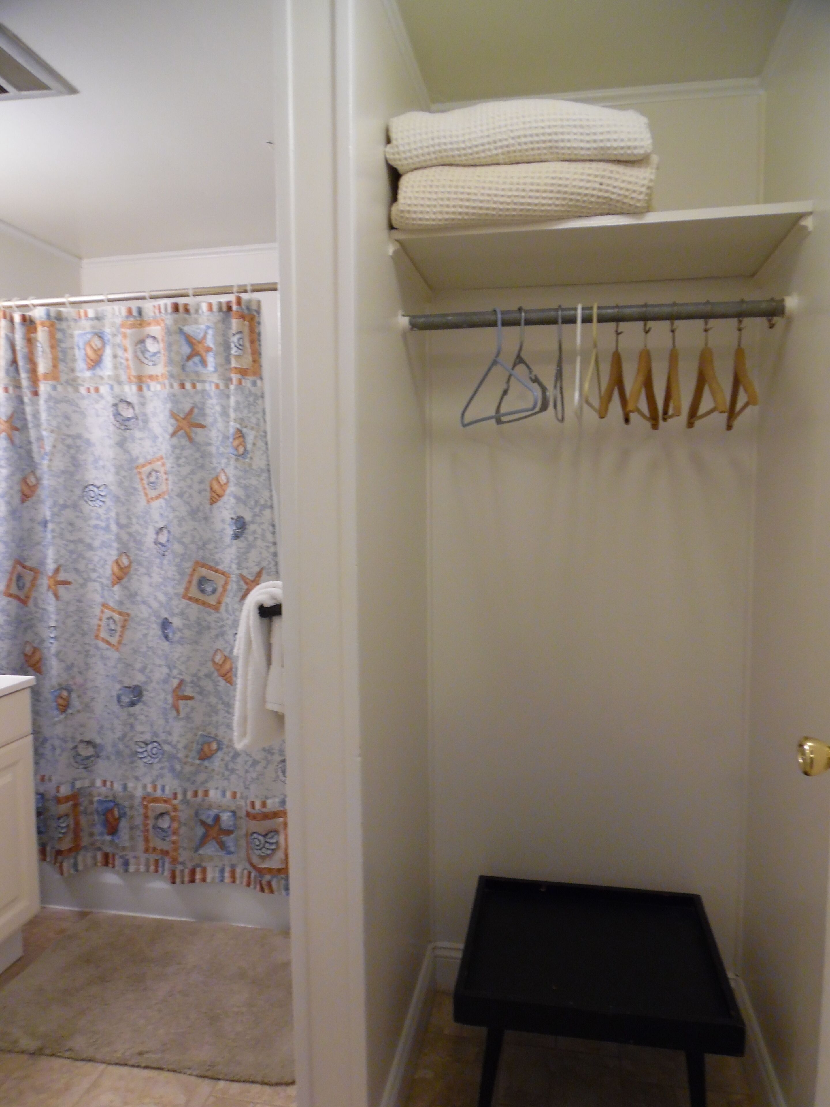 Ein Badezimmer mit Duschvorhang, Handtuchhalter mit Kleiderbügeln und einer kleinen Sitzbank.