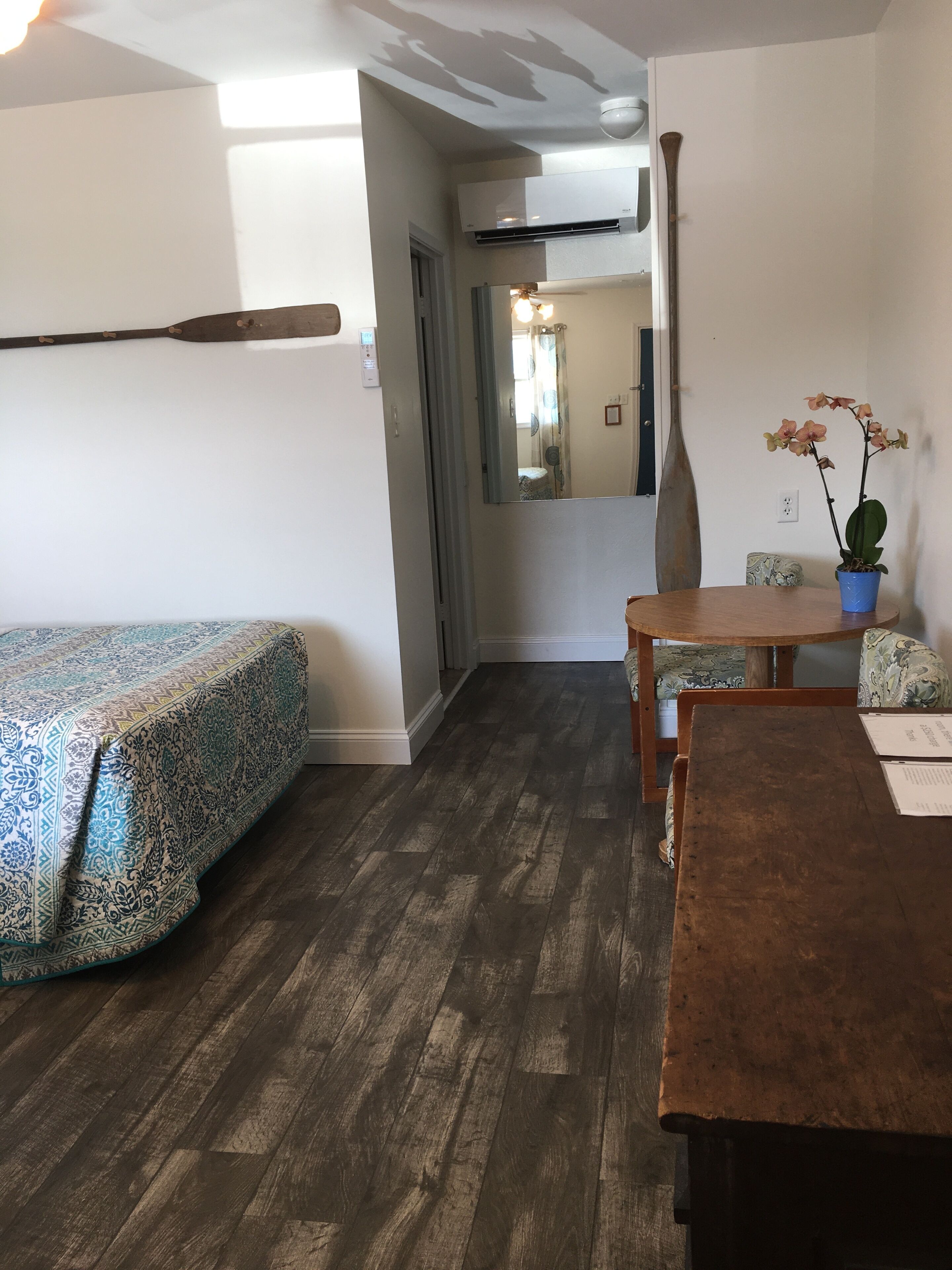 Une pièce comprenant un lit, une table en bois, une chaise, un pot d’orchidée et un miroir.