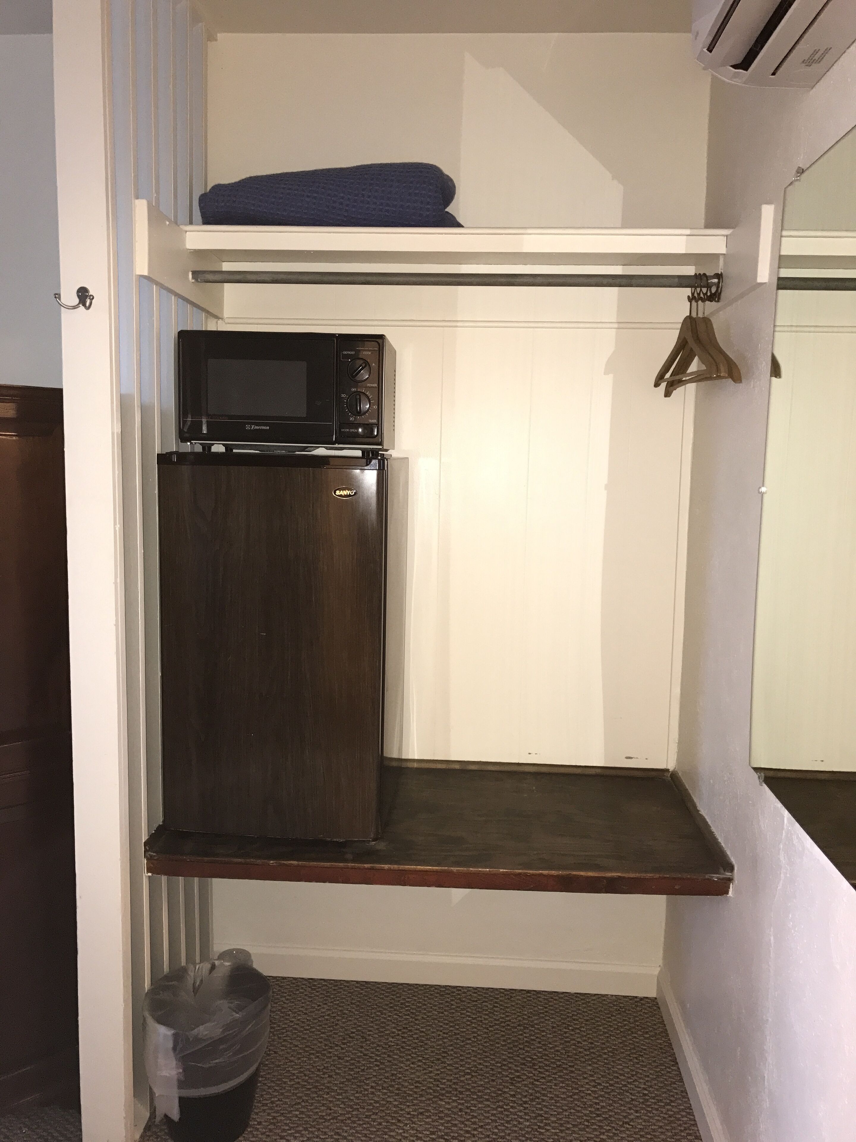A compact kitchenette with a microwave, refrigerator, and a small shelf.