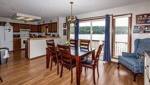 A spacious kitchen with wooden cabinets, a dining table with chairs, and a view of a lake through large windows. - 13397 - 17 Aldaya Lane (Hot Springs)