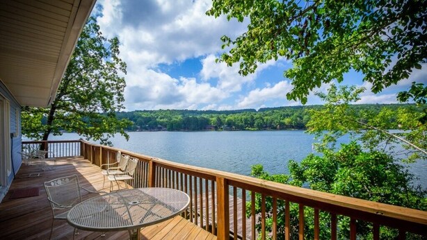 A wooden deck with a table and chairs, overlooking a lake with trees and hills in the background. - 13397 - 17 Aldaya Lane (Hot Springs)