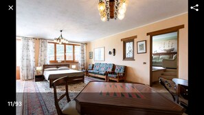 A room with a bed, a sofa, a dining table, and a chandelier.