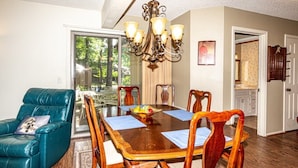 Un coin repas avec une table en bois, quatre chaises, un lustre et une vue sur l’extérieur, accessible par une porte vitrée.