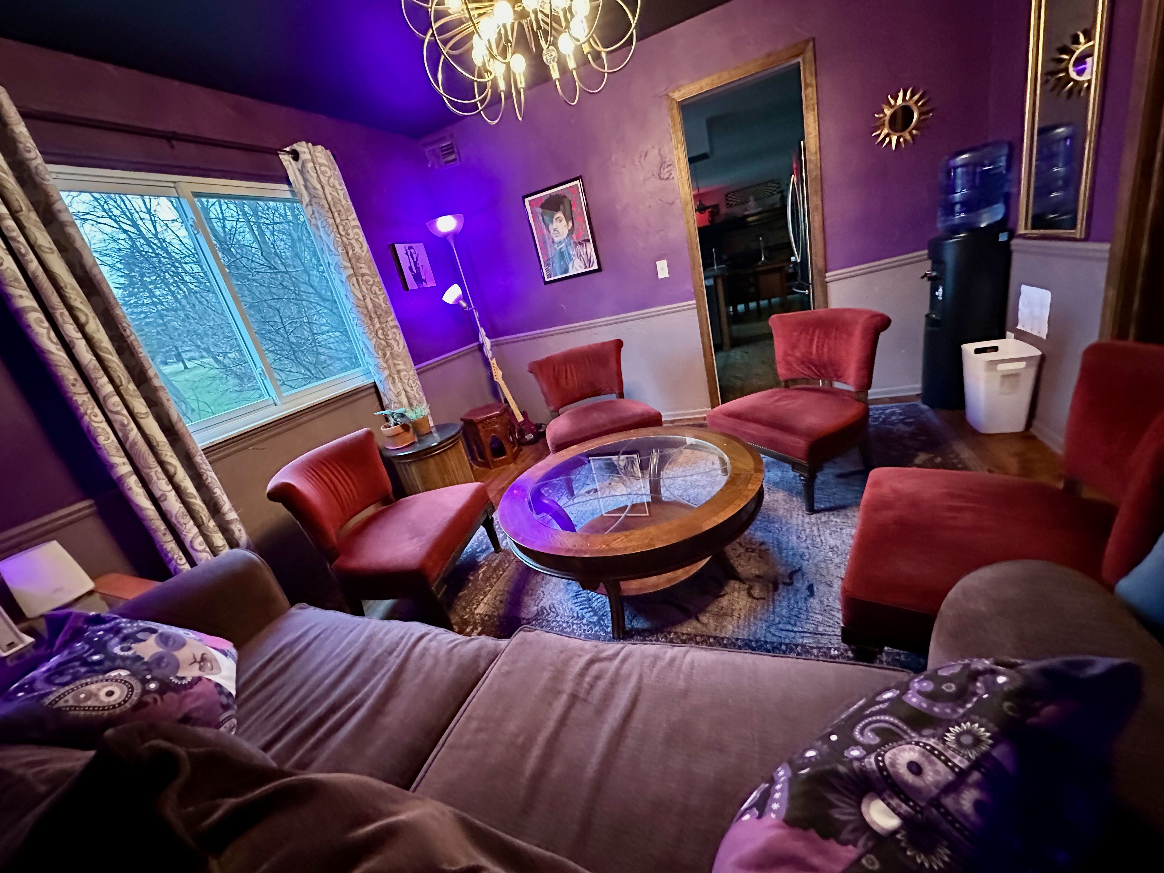 A living room with a round coffee table, red chairs, a sofa, and a large window with curtains.