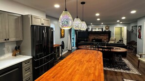 Una cucina moderna con isola in legno, elettrodomestici in acciaio inossidabile, illuminazione a sospensione e un'area pranzo con tavolo e sedie rotonde.