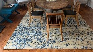 Un comedor con una mesa redonda de madera, cuatro sillas, una araña y una escalera al fondo.
