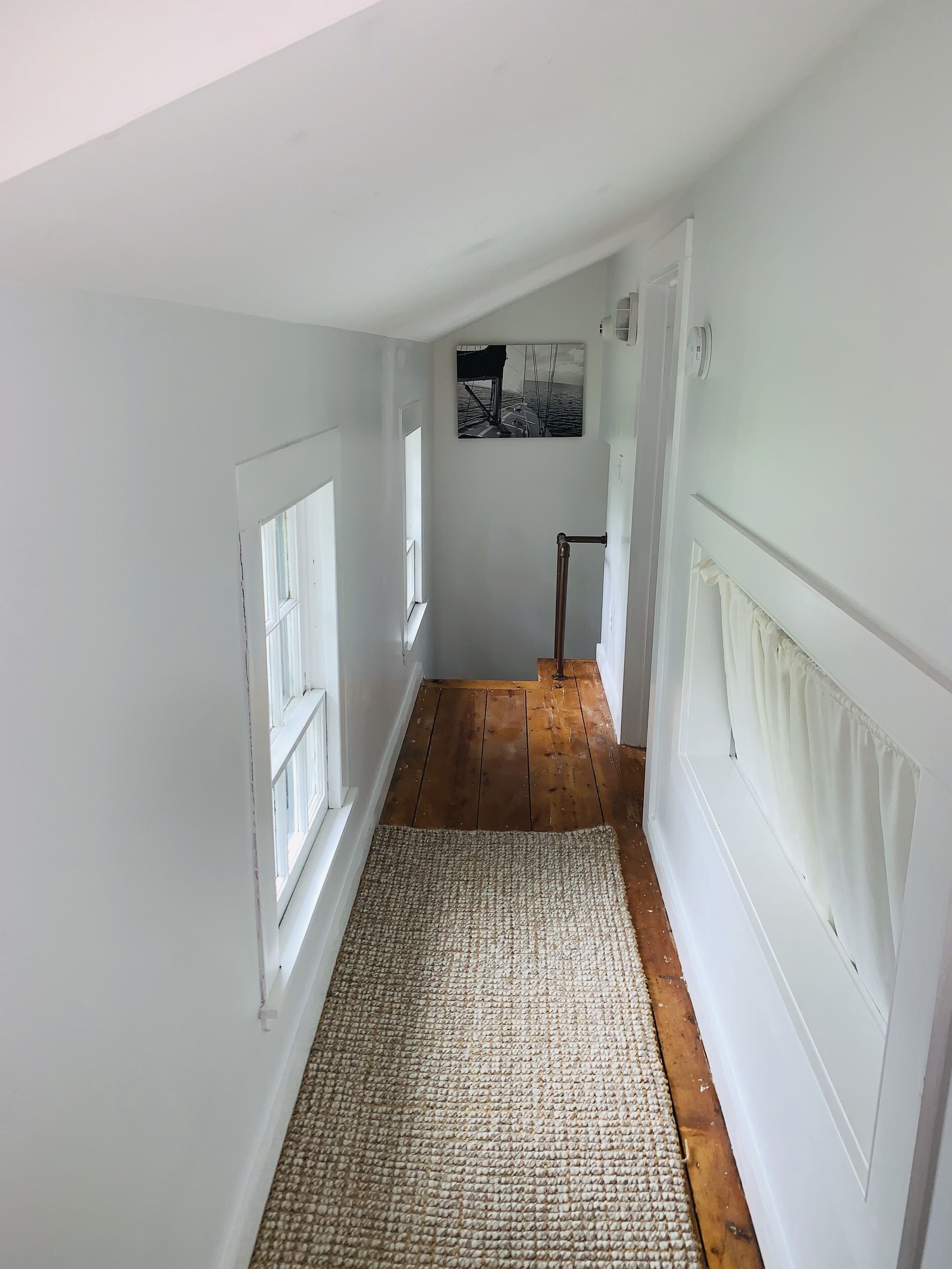 A narrow hallway with wooden flooring, white walls, and a textured rug.
