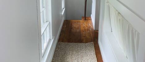 A narrow hallway with wooden flooring, white walls, and a textured rug.