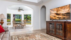 A spacious living room with a large TV, a fireplace, and a dining area with a view of a golf course. - 18810 - 10 Cruzado Lane (Hot Springs Village)