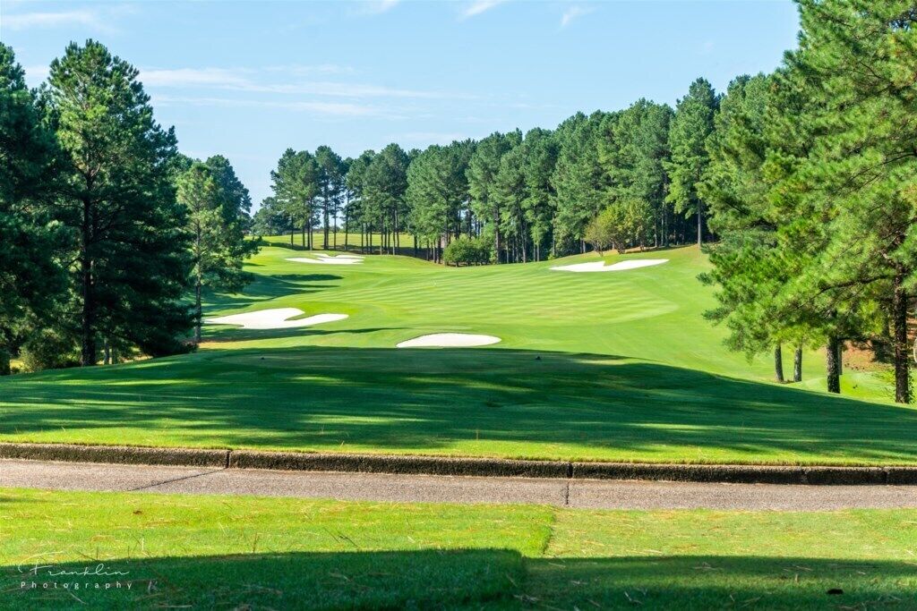Campo de golf con búnkeres de arena, árboles y cielo despejado.