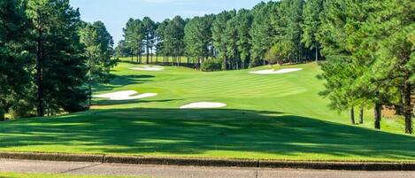 Campo de golf con búnkeres de arena, árboles y cielo despejado.